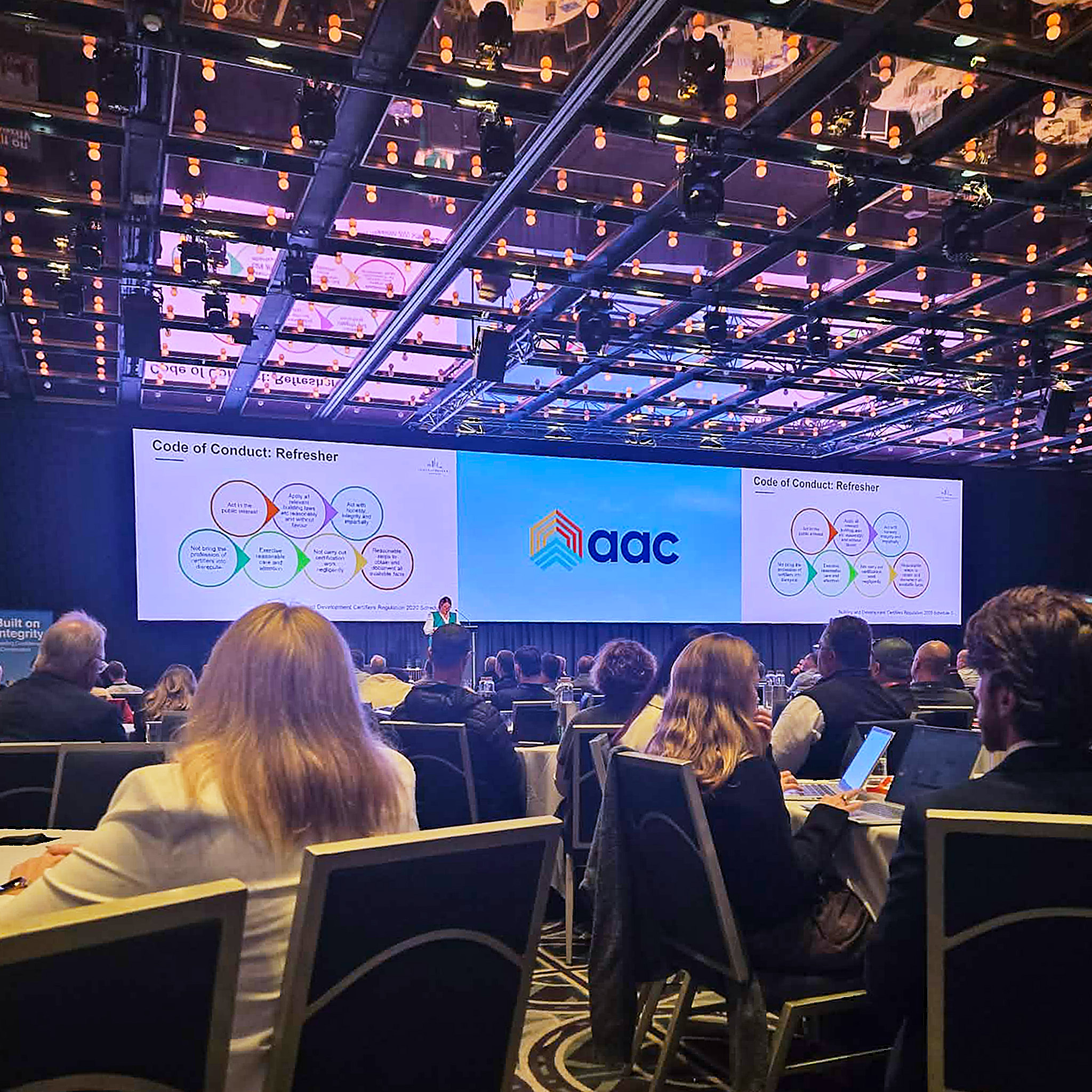 The view of huge screens on stage for the AAC presentations and conference as seen from the crowd at Sofitel Sydney Wentworth whilst attending a private certifier industry event in Sydney NSW