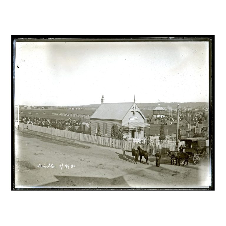 Historical black and white photograph from 1890 showing the wooden Lambton Council Chambers building, a crowd of people gathered on a grass field, horse-drawn carriages, and a picket fence.
