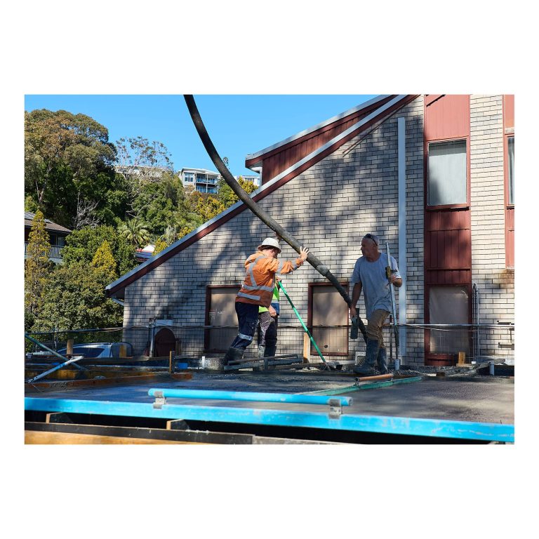 Concreters guiding a flexible pump hose and spreading wet concrete across reinforced steel and formwork for a modern house build in Merewether.