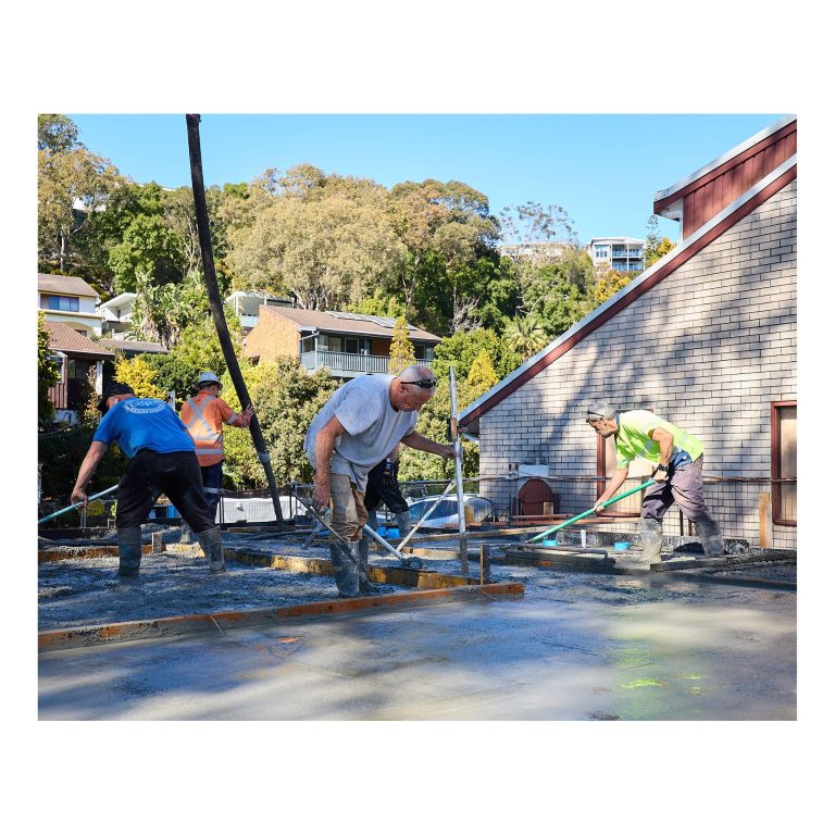 Construction workers using screeds and hand floats to level out freshly poured concrete on a residential building site in Merewether NSW.