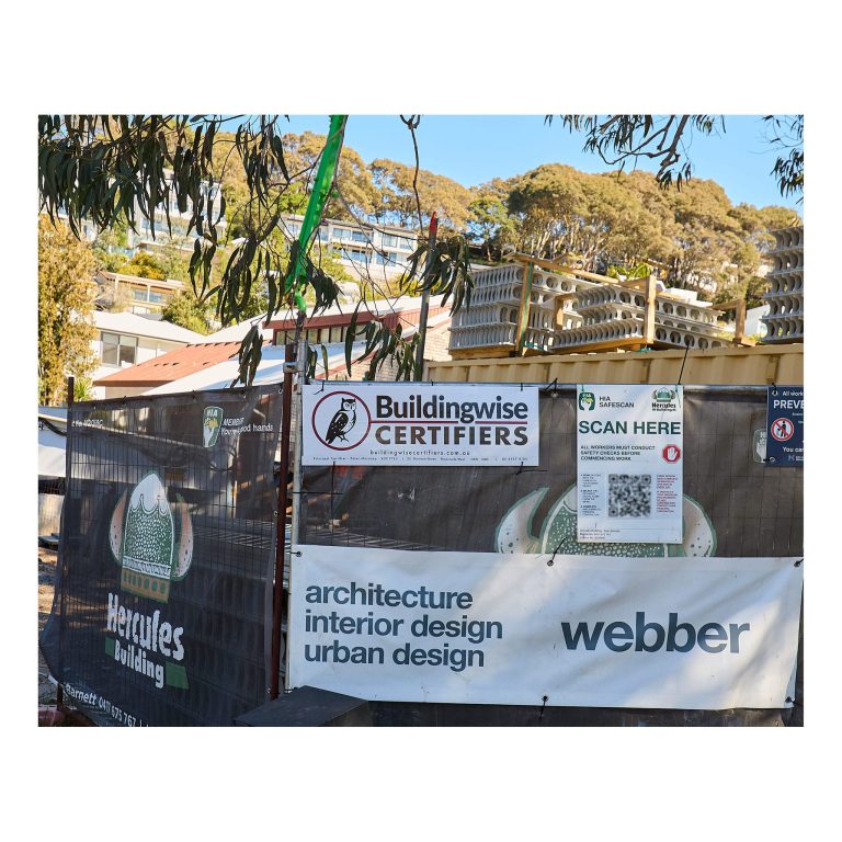 Close-up of a construction site fence in Merewether featuring promotional signage for Buildingwise Certifiers, Hercules Building, and Webber Architecture.